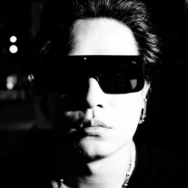 黒い服とサングラスを身につけたAI Media Studio運営者のモノクロ写真